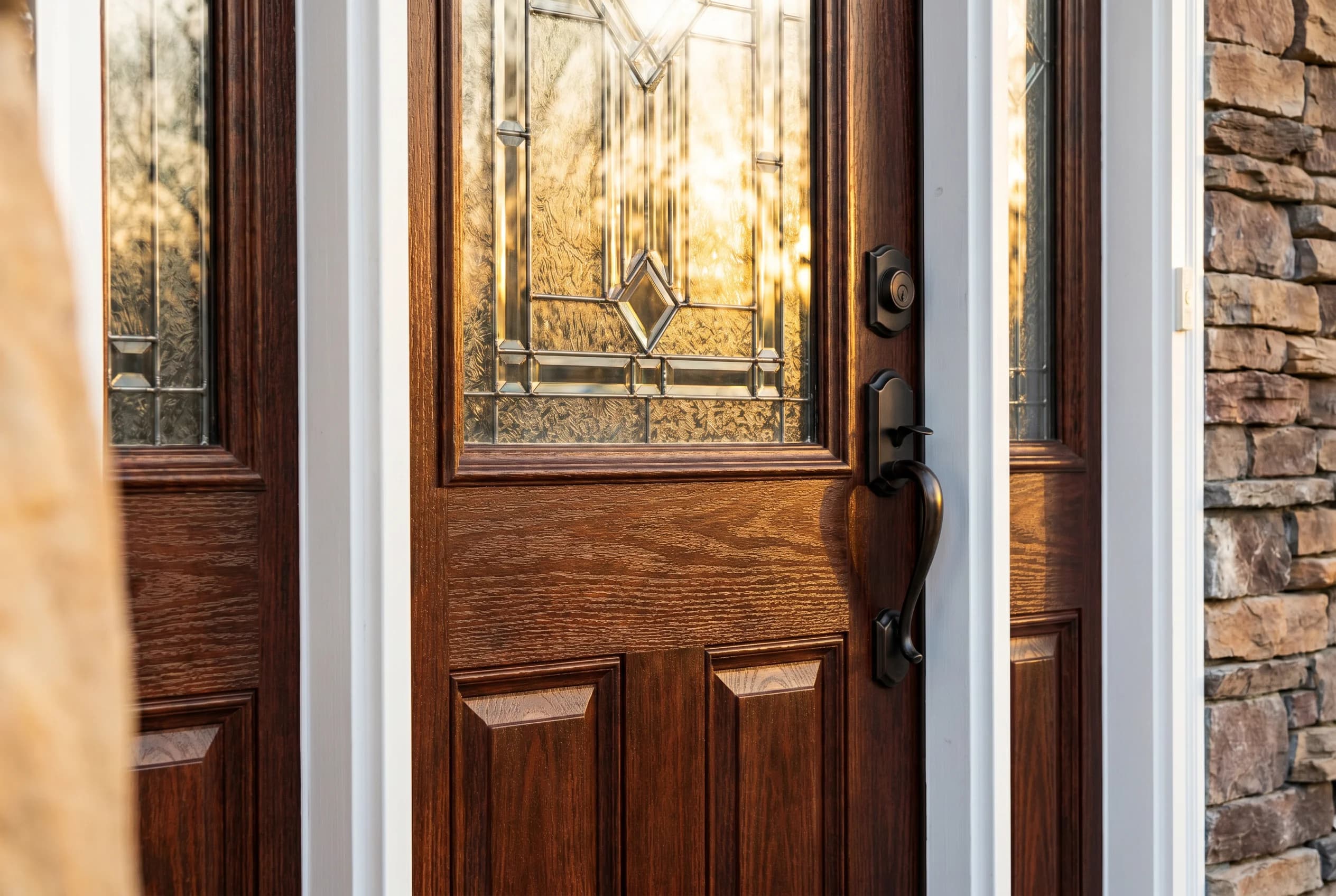 Brand-new ProVia Heritage premium fiberglass entry door with matching sidelights, deep mahogany wood-grain finish, premium oil-rubbed bronze hardware, stone accent backdrop