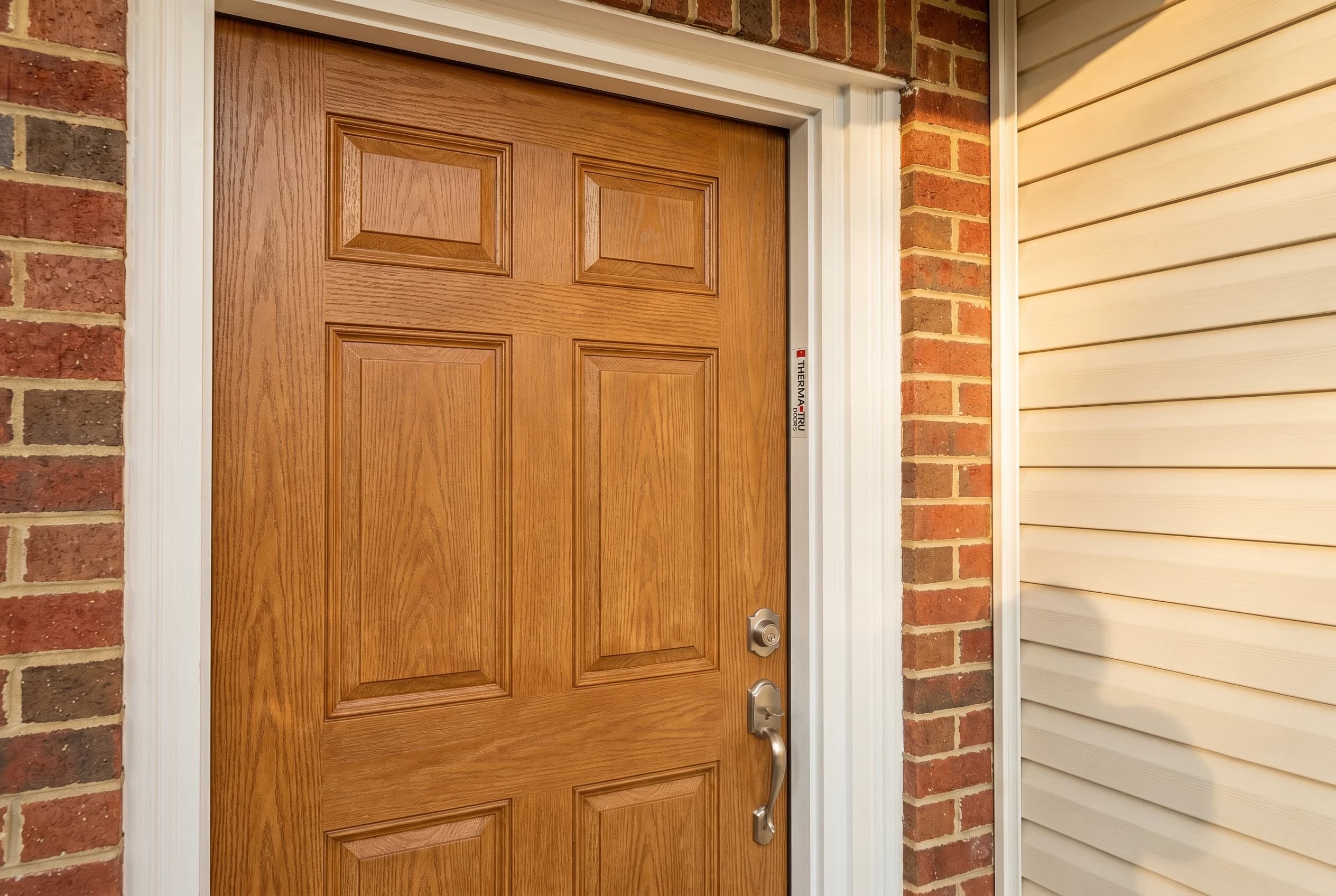 Brand-new Therma-Tru Fiber-Classic mid-tier fiberglass door with embossed oak wood-grain texture, honey-stained finish, six-panel traditional design
